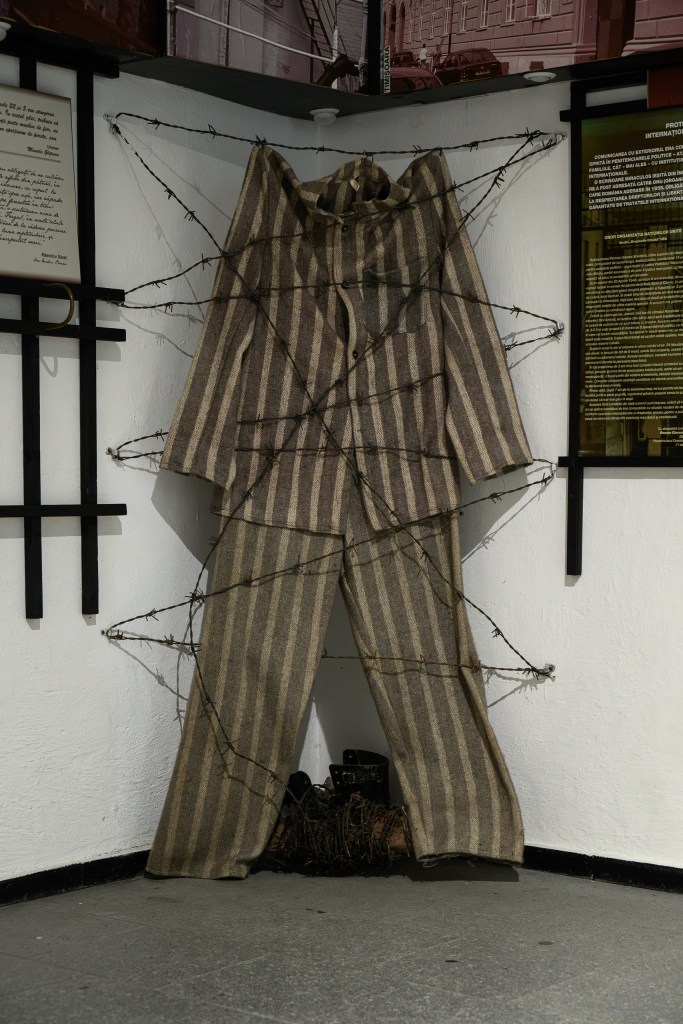 A striped prisoner's uniform displayed on a wall, wrapped in barbed wire, symbolizing confinement and suffering.