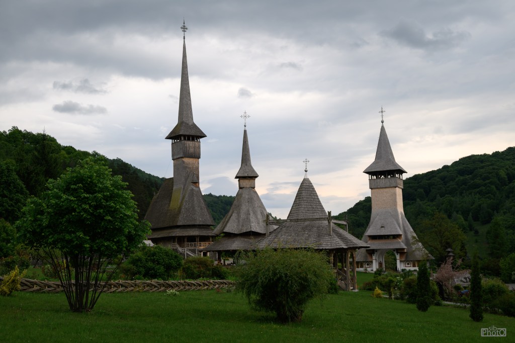 A picturesque landscape featuring traditional wooden churches with tall spires, surrounded by lush greenery and under a cloudy sky.